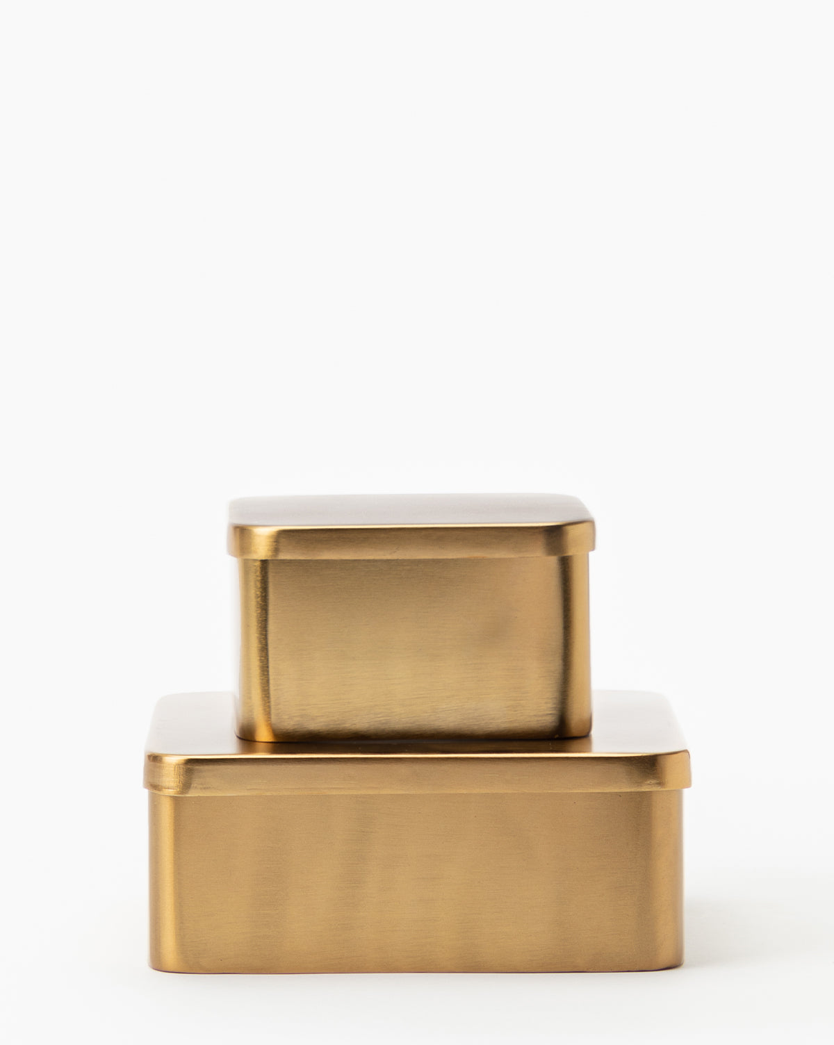 Two Oswald Metal Boxes with a brass finish are stacked against a white background. The smaller box sits centered on the larger one, highlighting their sleek metallic gold color and minimalist design.