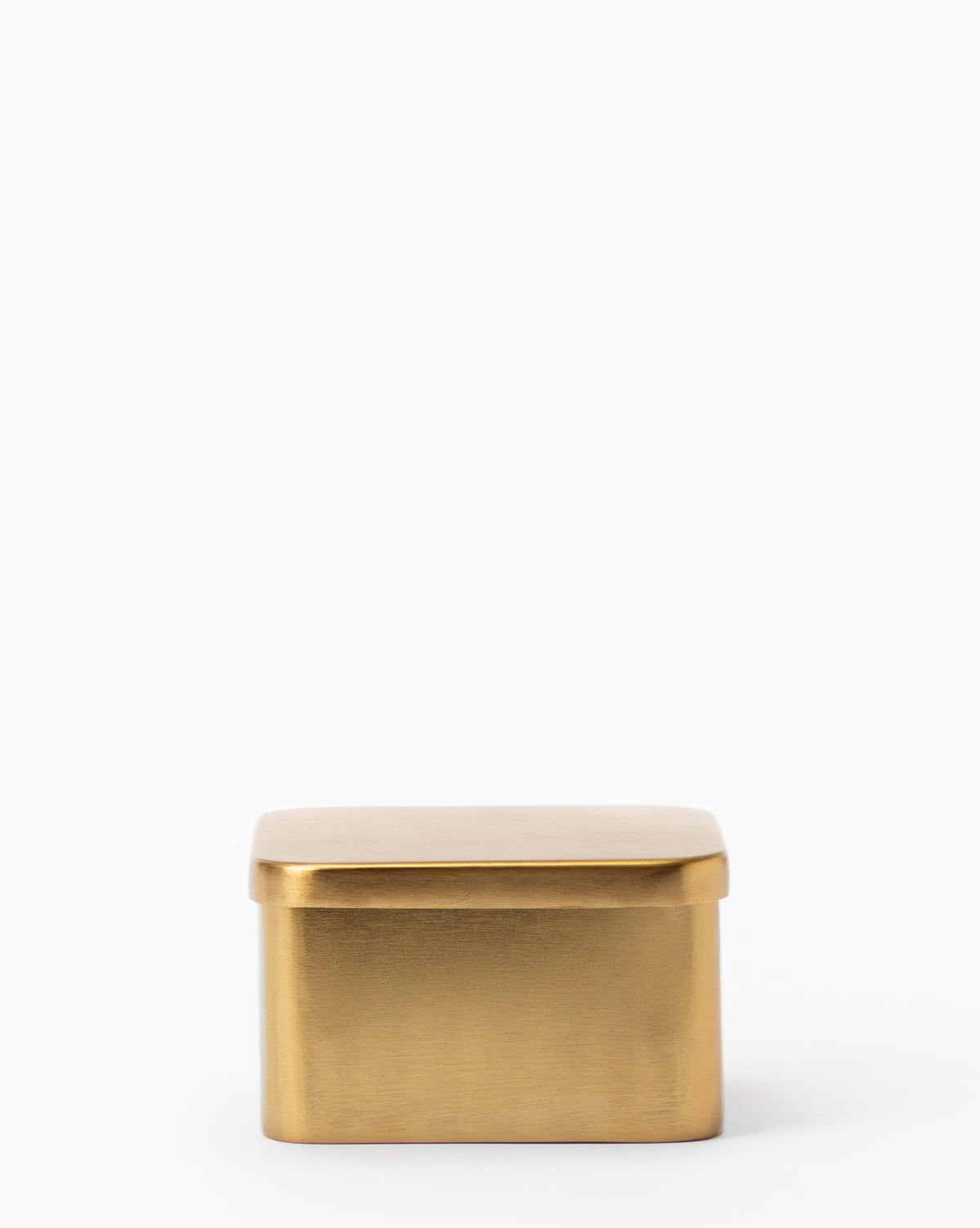 The Oswald Metal Box is a small, rectangular box with a brass finish, rounded edges, and a fitted lid. Its minimalist design stands out against a plain white background.