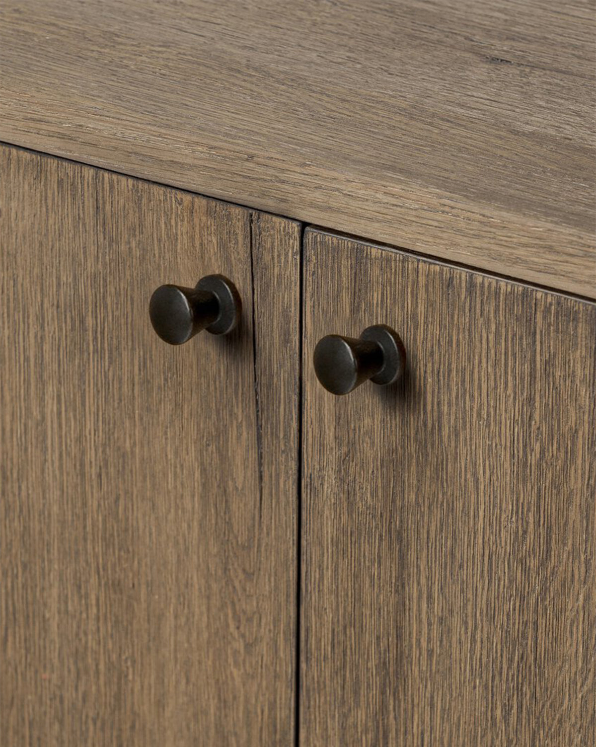 Close-up of two wooden cabinet doors on the Oswin Sideboard, featuring a weathered oak finish with light brown wood grain and round, dark metal knob handles, by McGee & Co.