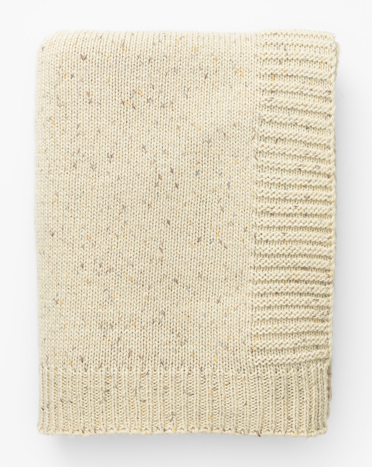 The Otis Knit Throw by Makerspalm is a cream-colored wool blend with ribbed edges and subtle grey-speckled brown and tan flecks, neatly folded and displayed on a white background. McGee & Co.