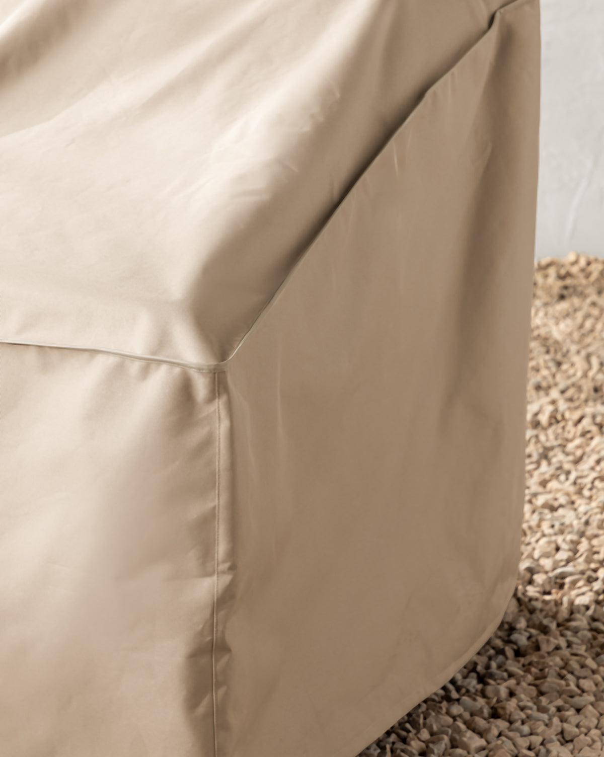 Close-up of a beige Outdoor Lounge Chair Cover, water-resistant, draped over a square-shaped object and resting on light-colored pebbles by McGee & Co.