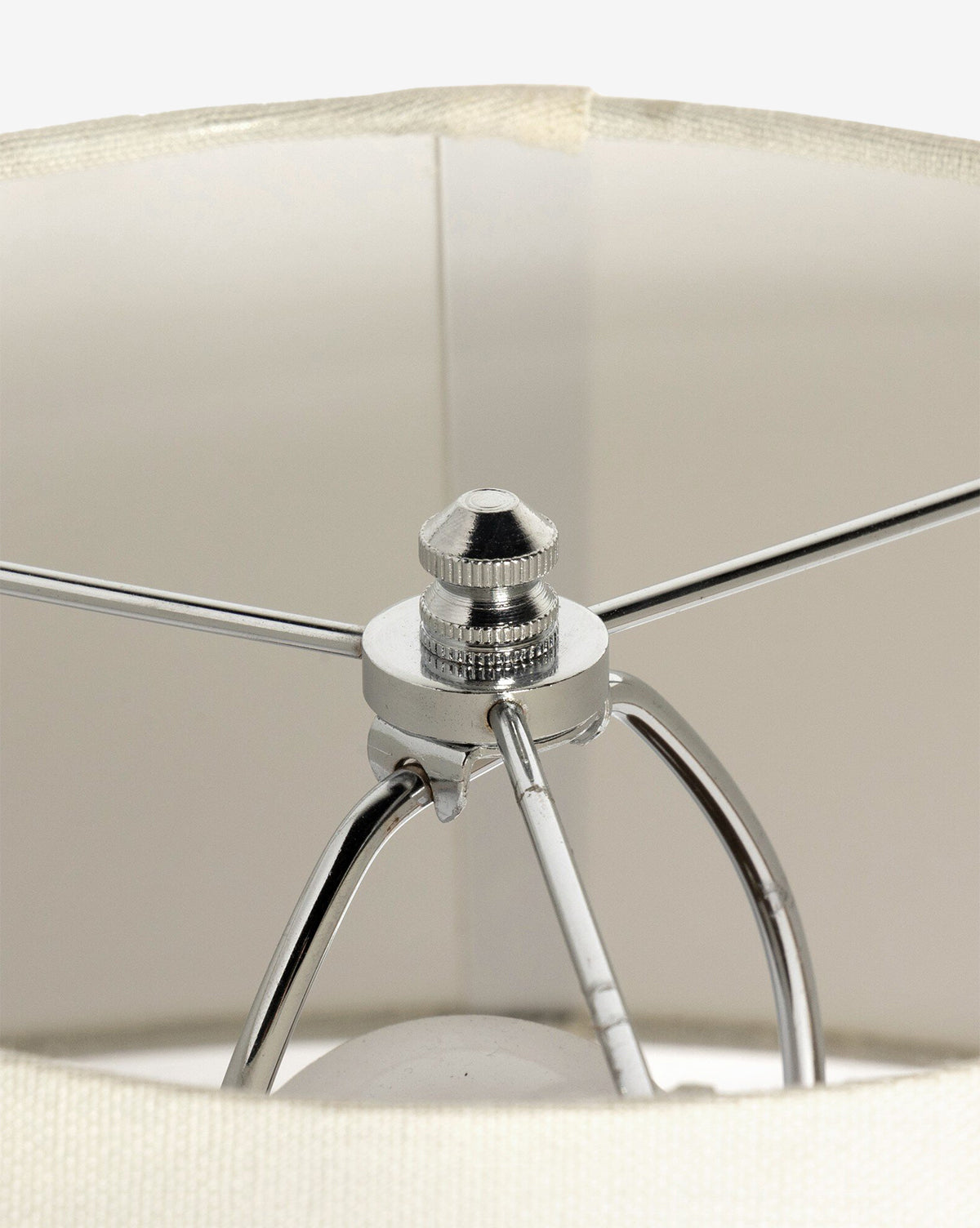 Close-up of the ivory linen shade from the Parma Table Lamp, showing its metal frame with arms meeting at a central finial. The lamp’s bulb is partially visible below against a white background, by McGee & Co.