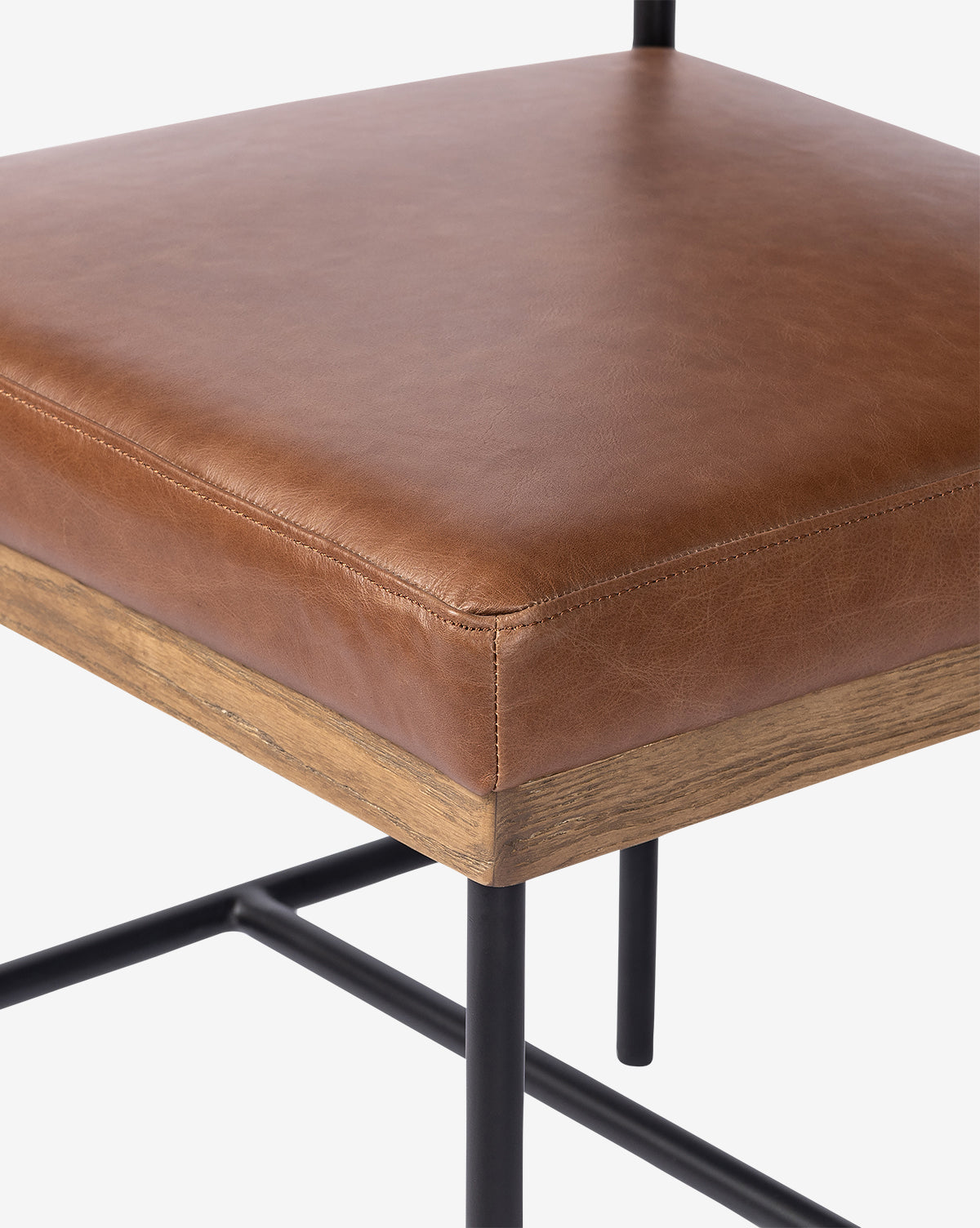 Close-up of the Pascal Dining Chair with a brown leather cushioned seat, wooden trim, and black steel and wood legs with a crossbar—an ideal addition to any dining table setting, by McGee & Co.