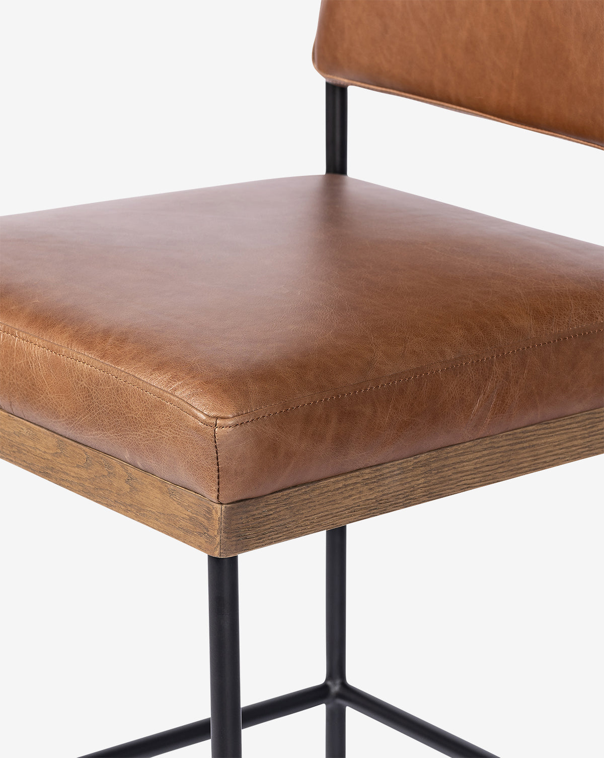 Close-up of the Pascal Stool featuring a light brown leather seat and backrest, wooden edges, and a black iron frame, displayed against a plain white background, by McGee & Co.