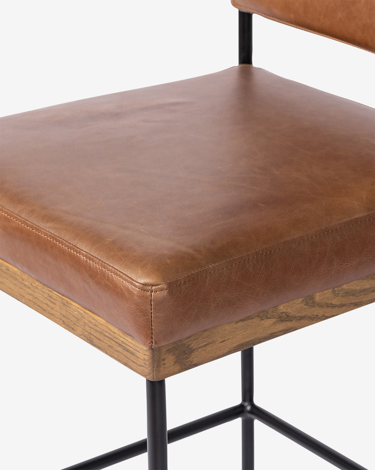 Close-up of the Pascal Stool seat with brown leather upholstery, wooden trim at the base, and a black iron frame. This versatile stool features a modern industrial design, by McGee & Co.