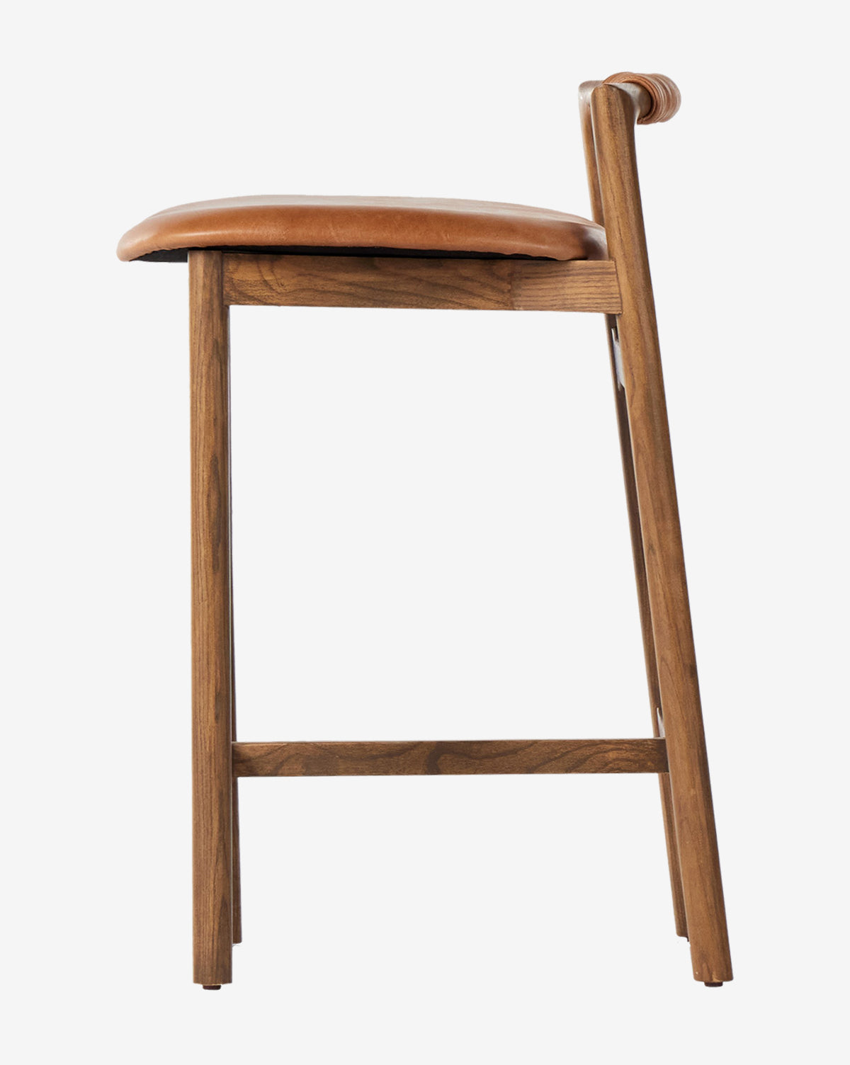 A side view of the Four Hands Patrin Stool, featuring a performance upholstered seat and ash wood frame, displays its modern, minimalist design against a plain white background. McGee & Co.