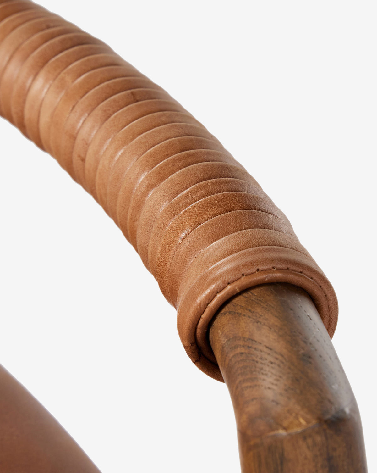 Close-up of a Four Hands Patrin Stool’s ash wood frame armrest, wrapped in smooth light brown leather strips with detailed stitching and texture, set against a plain white background. McGee & Co.