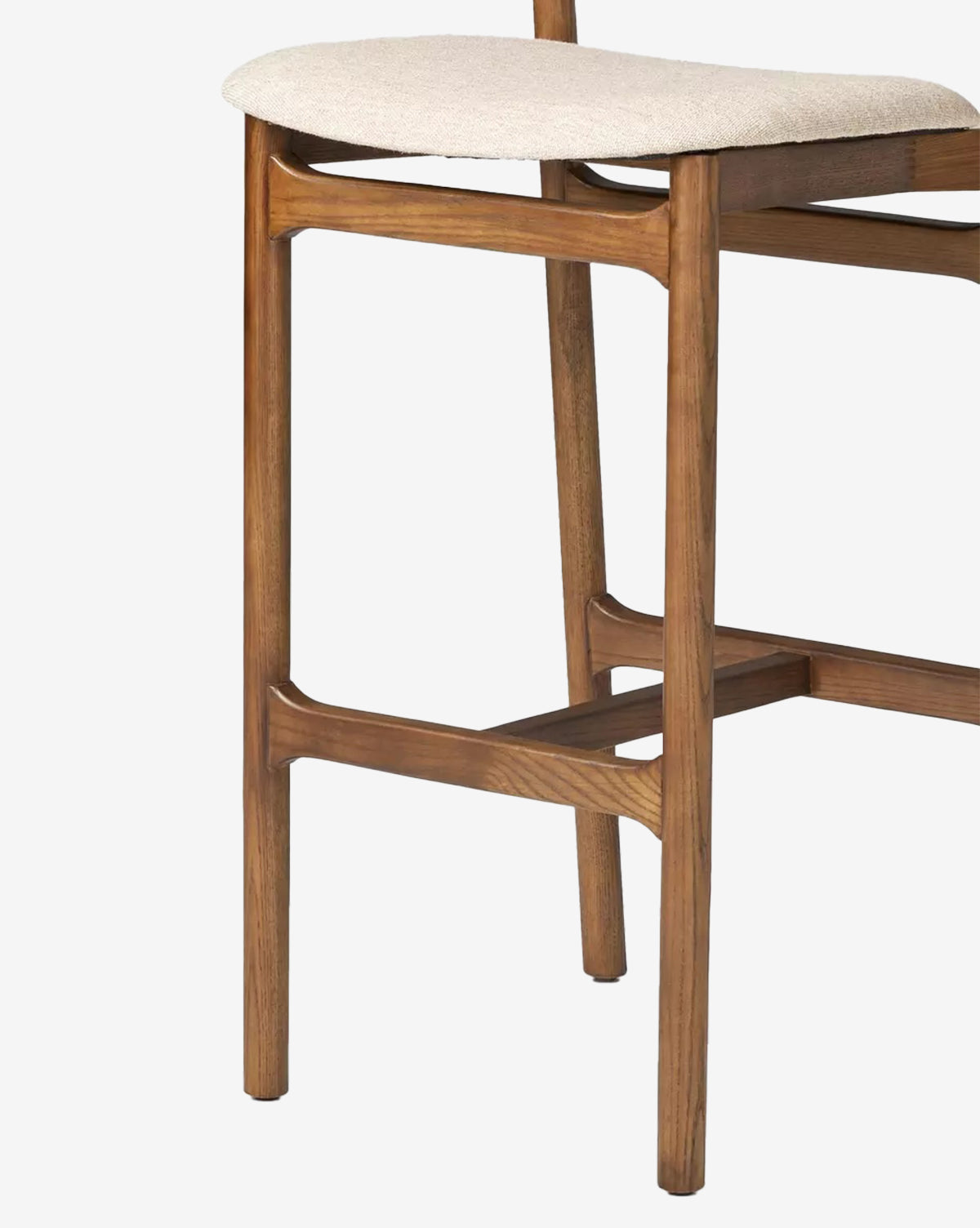 A close-up of the Four Hands Patrin Stool shows its ash wood frame and beige performance-upholstered seat, featuring a mid-century modern design with smooth, rounded edges and visible joinery. McGee & Co.