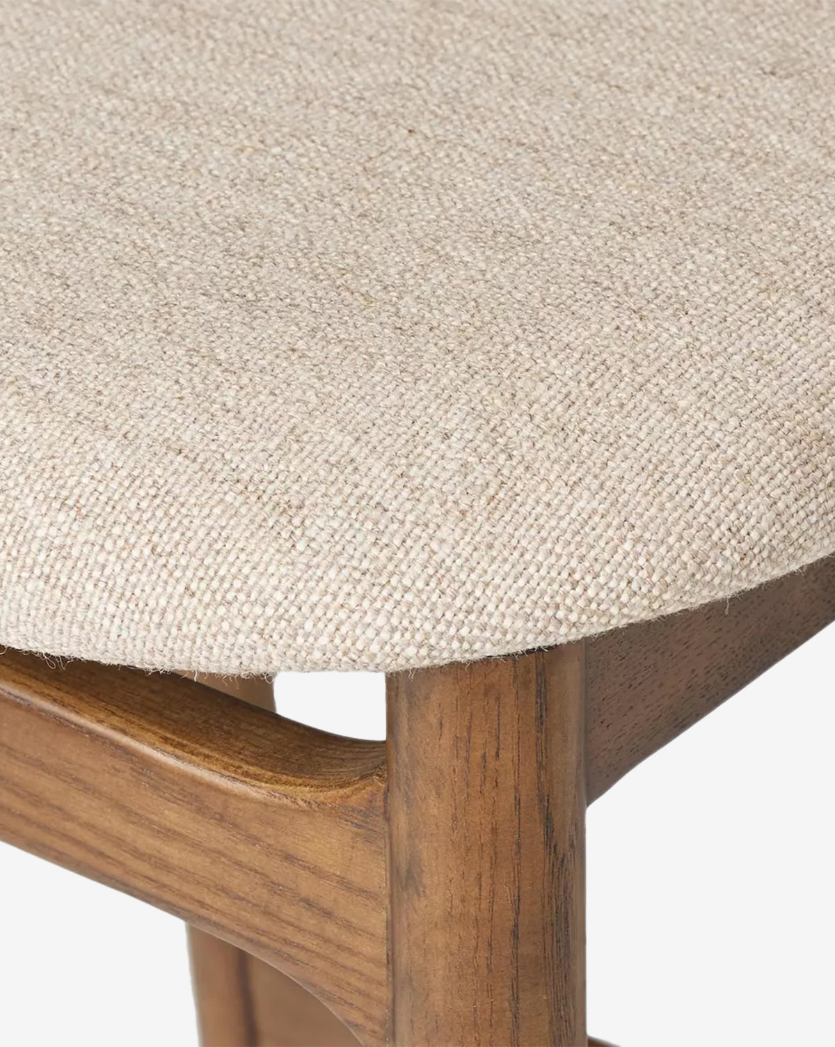 Close-up of the Four Hands Patrin Stool, featuring its performance-upholstered seat in beige woven fabric and displaying the ash wood frame and leg beneath. McGee & Co.