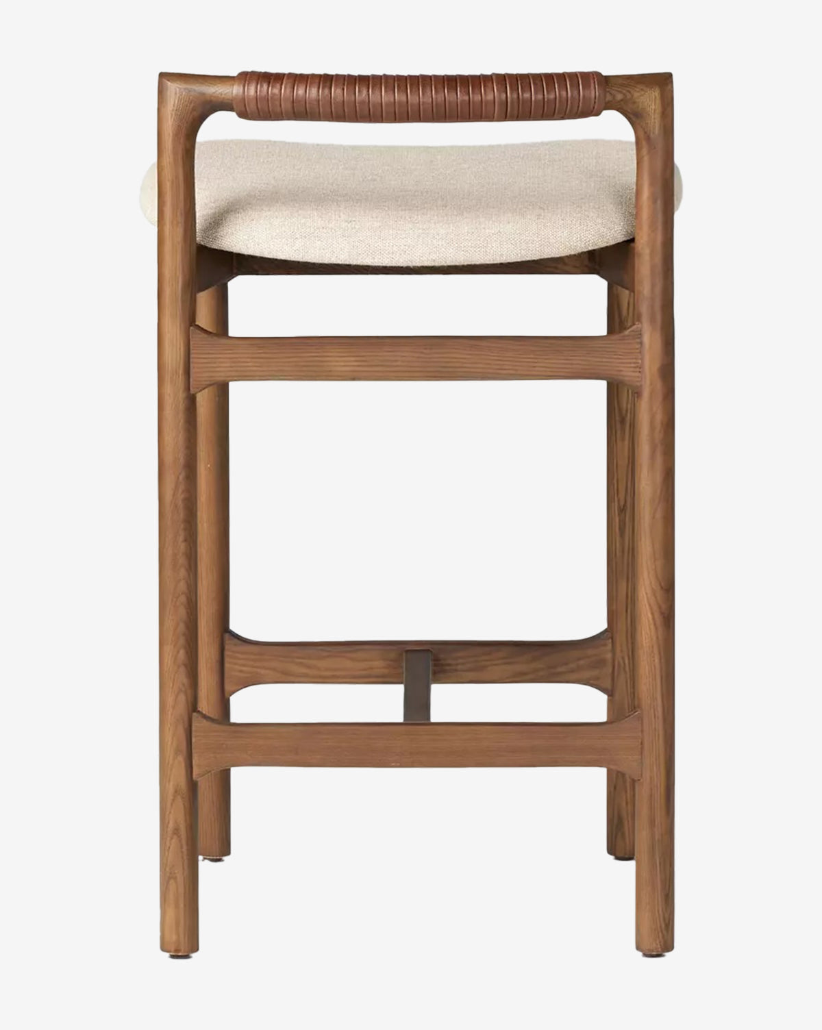 The Patrin Stool by Four Hands features an ash wood frame, light beige performance upholstery, a footrest, and a brown leather-wrapped backrest, shown from behind against a white background. McGee & Co.