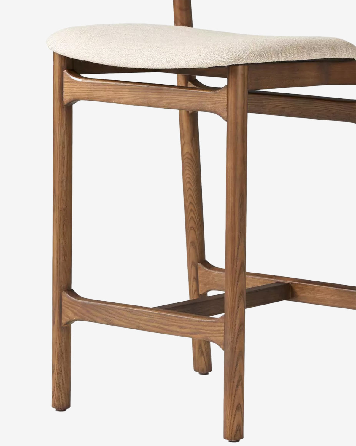 A close-up of the Four Hands Patrin Stool highlights its performance light beige upholstered seat, minimalist design, and medium-toned ash wood legs and frame with visible grain, McGee & Co.
