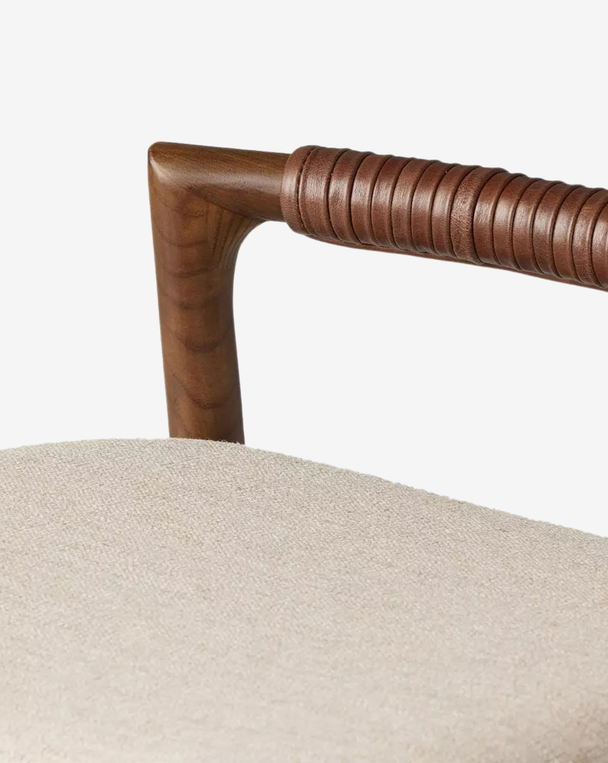 Close-up of a Four Hands Patrin Stool’s dark ash wood armrest wrapped in brown leather, with a light beige performance seat, set against a plain white background. McGee & Co.