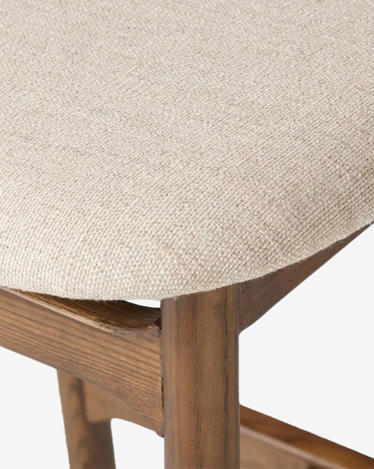 Close-up of the Patrin Stool by Four Hands, showcasing its beige textured performance upholstery and sturdy ash wood frame in a natural brown finish, with details of the seat and leg joint visible. McGee & Co.
