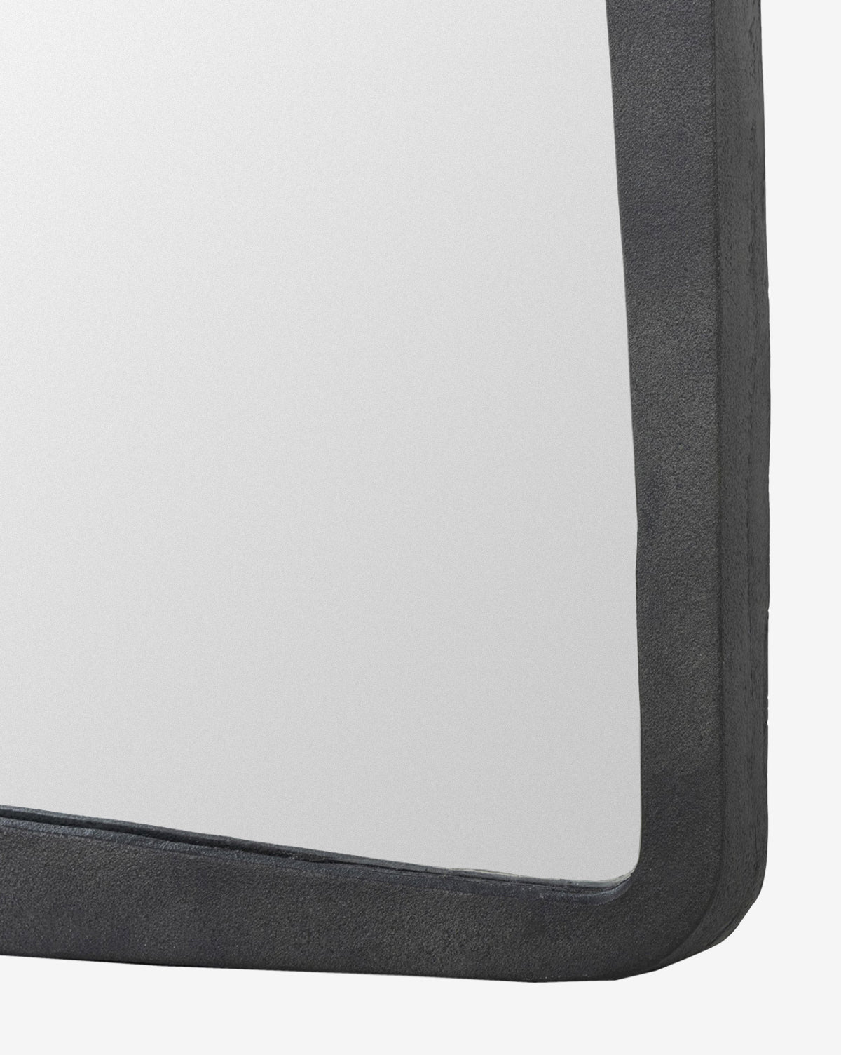 Close-up of the top right corner of the Penrod Floor Mirror, featuring a thick, dark, textured cast aluminum frame. The mirror reflects a plain, light background—blending function and sculptural style in home decor, by McGee & Co.