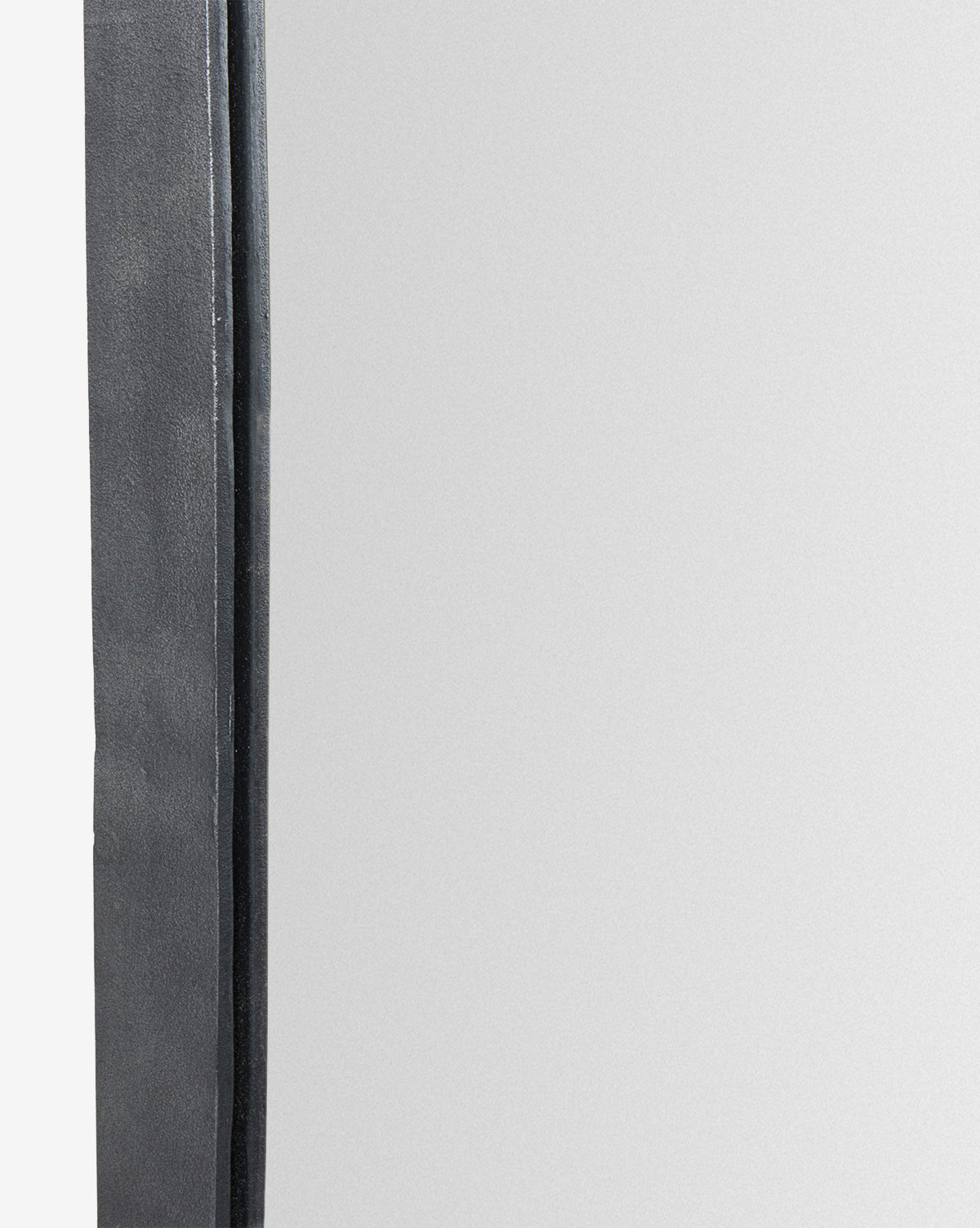 A close-up of the Penrod Floor Mirror shows its dark, textured cast aluminum frame along the left edge, while the right side reflects a blank, light surface, by McGee & Co.