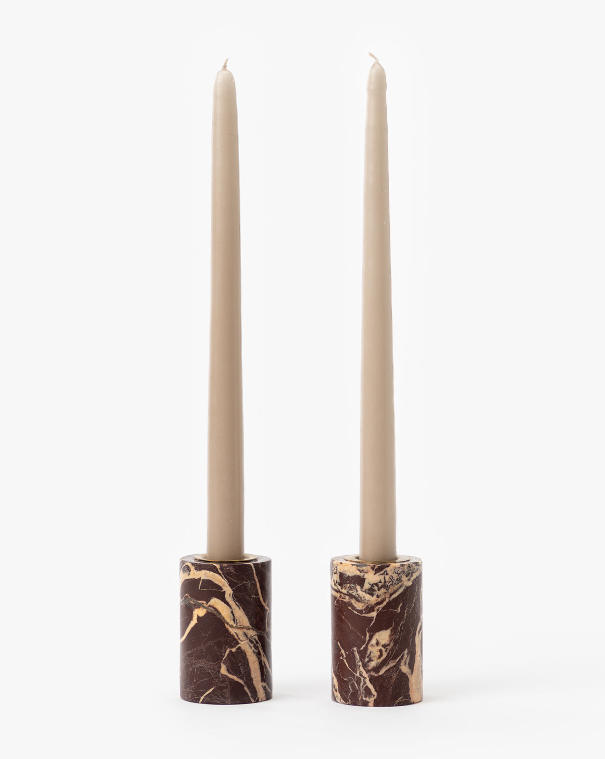 Two beige taper candles stand upright in Perrin Marble Taper Holders (Set of 2), each crafted from brown marble with gold and cream veining, accented by a subtle brass cap, all set against a plain white background.