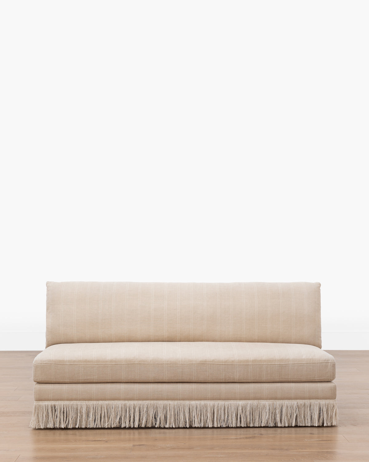 The Makerspalm Philippa Settee (Ready to Ship) features beige striped linen, a straight back, seat cushions, and decorative fringe at the base, shown on a wooden floor with a plain white background. McGee & Co.