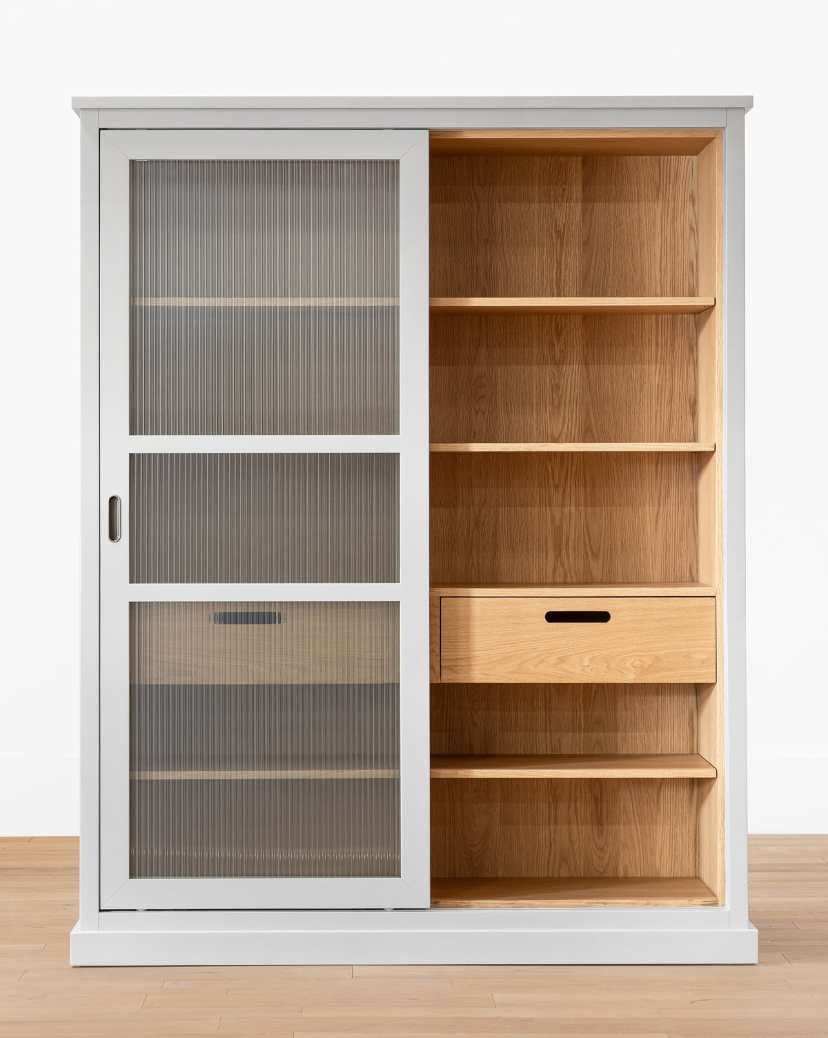 The Phillips Cabinet, made from painted oak, features a single sliding reeded glass door on the left, six open shelves, and two right-side drawers with antique brass handles, by McGee & Co.