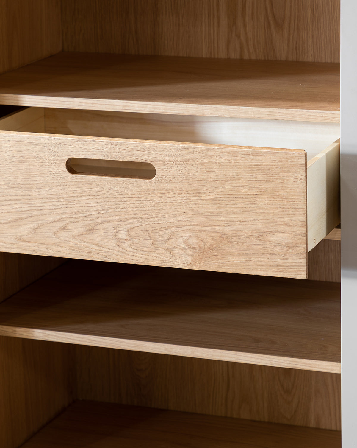 A close-up of the Phillips Cabinet shows a light oak pull-out drawer with a horizontal cutout handle, matching the unit’s shelves and interior, by McGee & Co. Reeded glass doors add elegance to the cabinet’s painted finish, by McGee & Co.