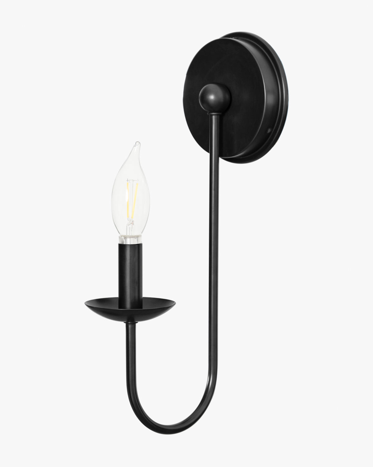 The Philomena Single Sconce by Makerspalm features a black metal frame with a round base and curved arm, holding an exposed candle-shaped bulb on a circular plate for modern wall lighting by McGee & Co.