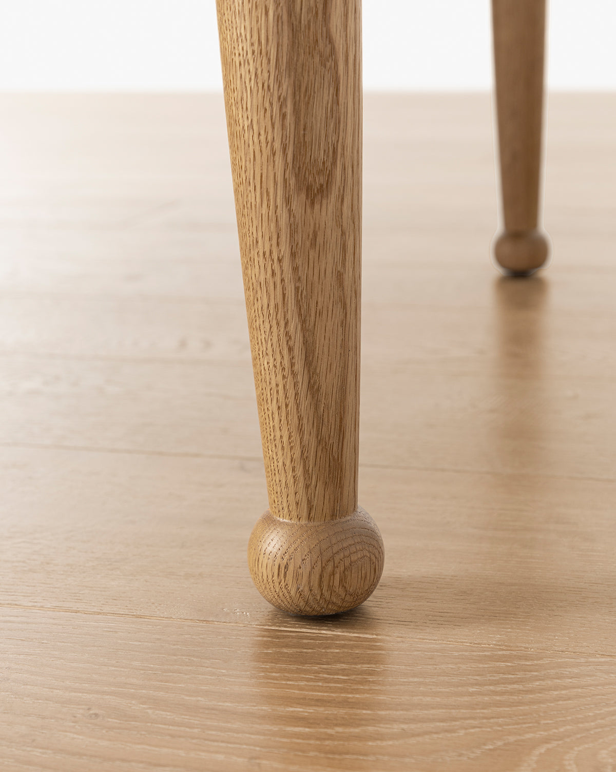 Close-up of two handcrafted Phipps Dining Table legs on a light wood floor, with one leg sharply focused and the other softly blurred in the background, by McGee & Co.