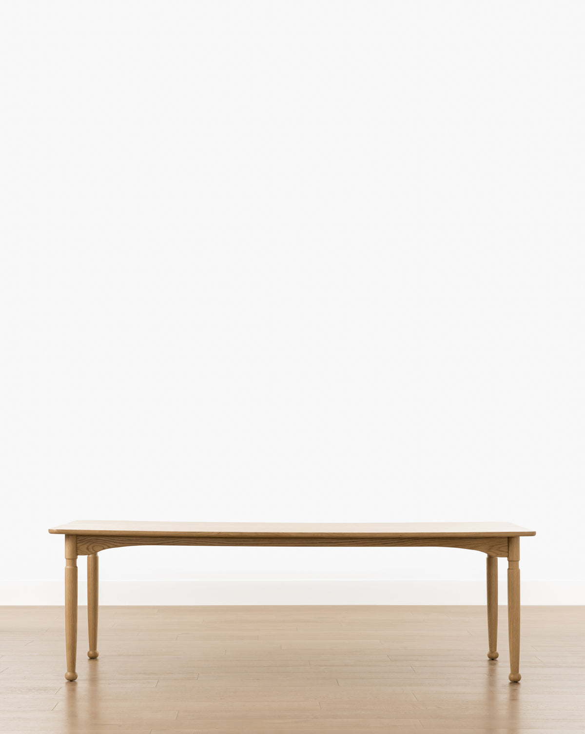 The Phipps Dining Table, handcrafted with four legs, is shown on a light wood floor against a plain white background by McGee & Co.