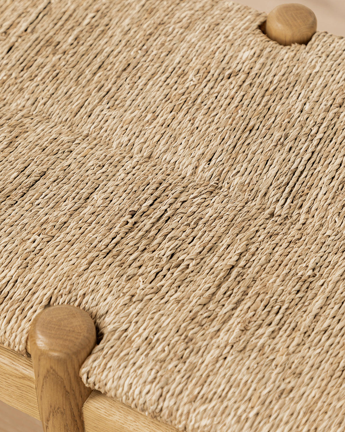 Close-up of the Phipps Woven Bench in honey oak, featuring a tightly interlaced natural fiber seagrass seat and rounded wooden corners, by McGee & Co.
