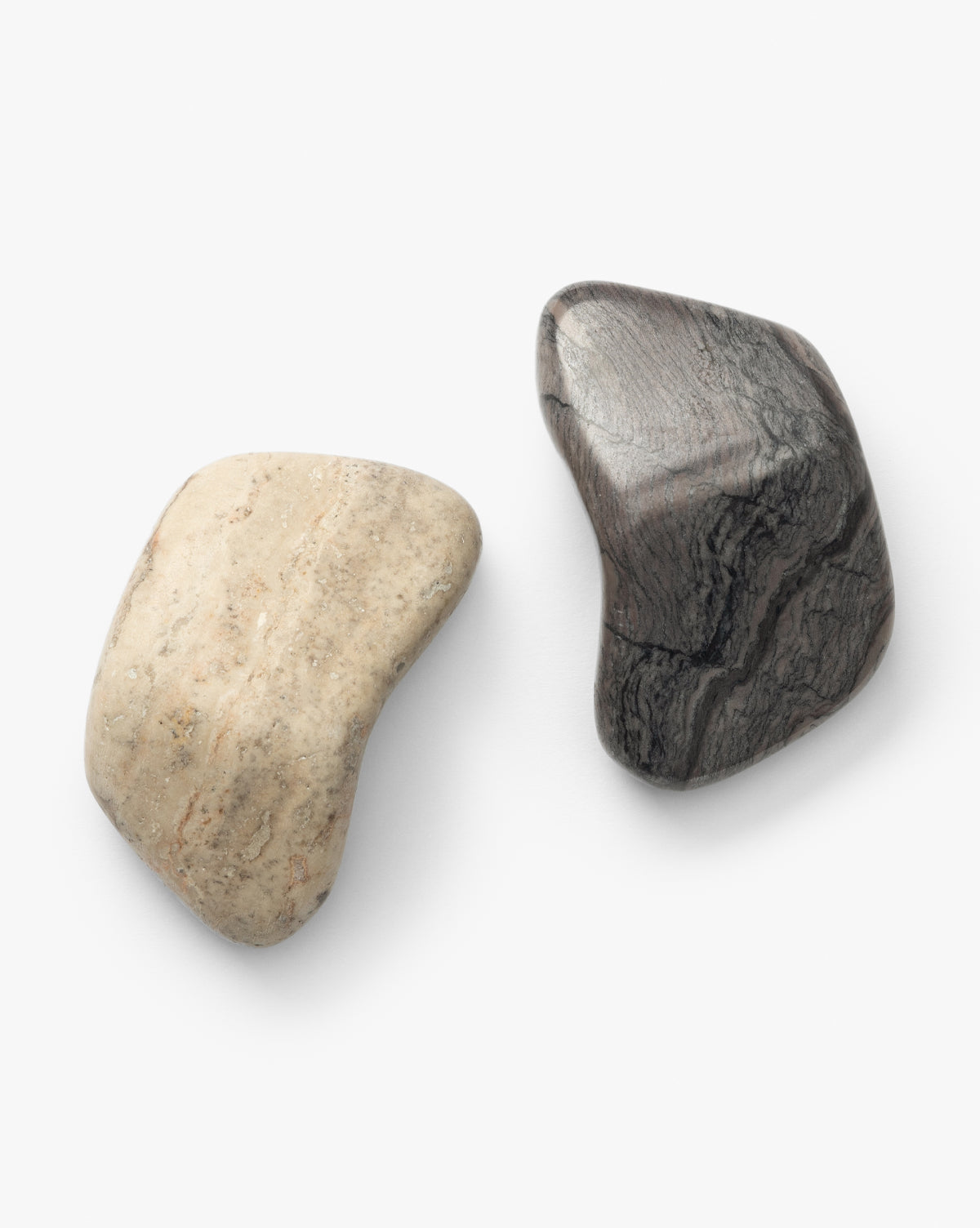 The Piedra Objects (Set of 2) feature two smooth, irregularly shaped stones—one light beige like silver travertine marble and one dark gray with wavy streaks—on a white background, perfect for coffee table styling, by McGee & Co.