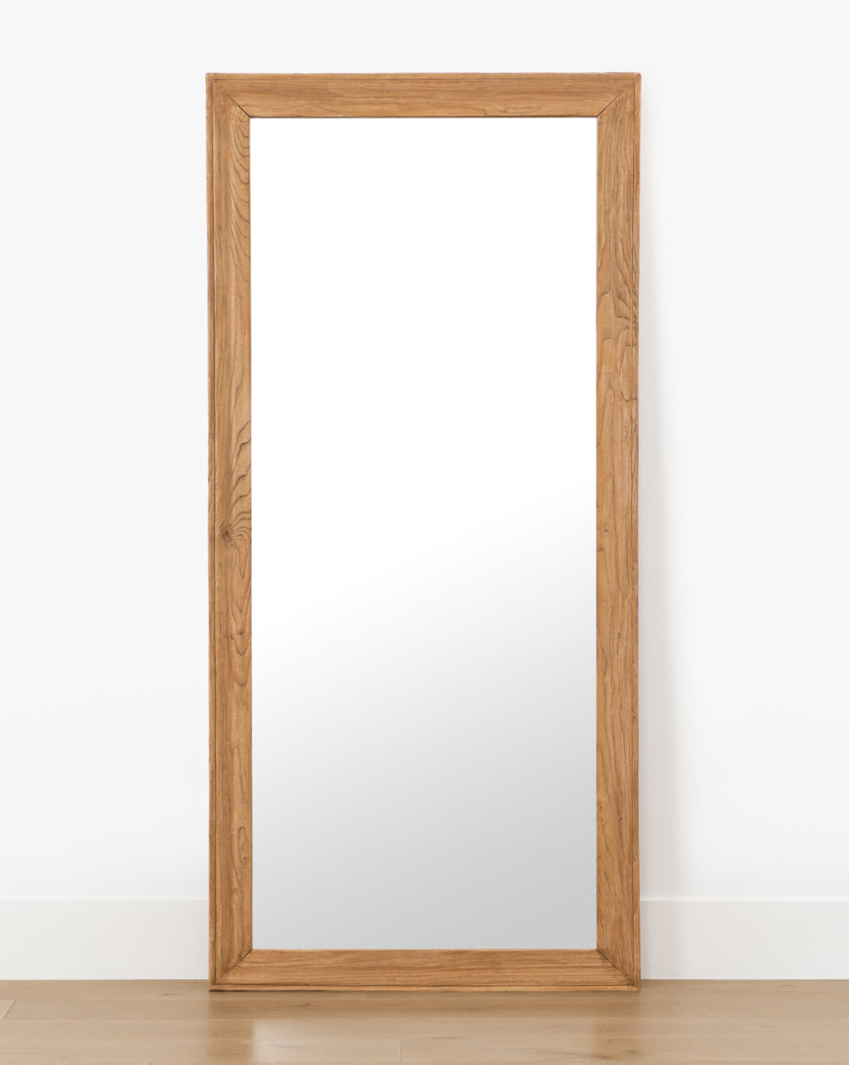 The Pippen Floor Mirror showcases a large rectangular shape and a natural wood frame in honey elm finish, perfect for leaning upright against any wall, by McGee & Co.