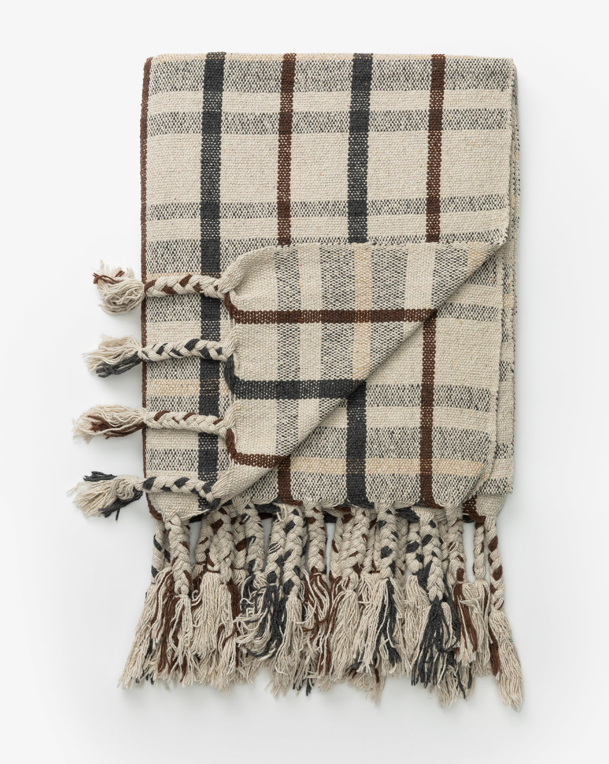 The Plaid Tasseled Throw in beige showcases a classic plaid pattern with black and brown accents and braided tassels on the edges, shown folded on a white background.
