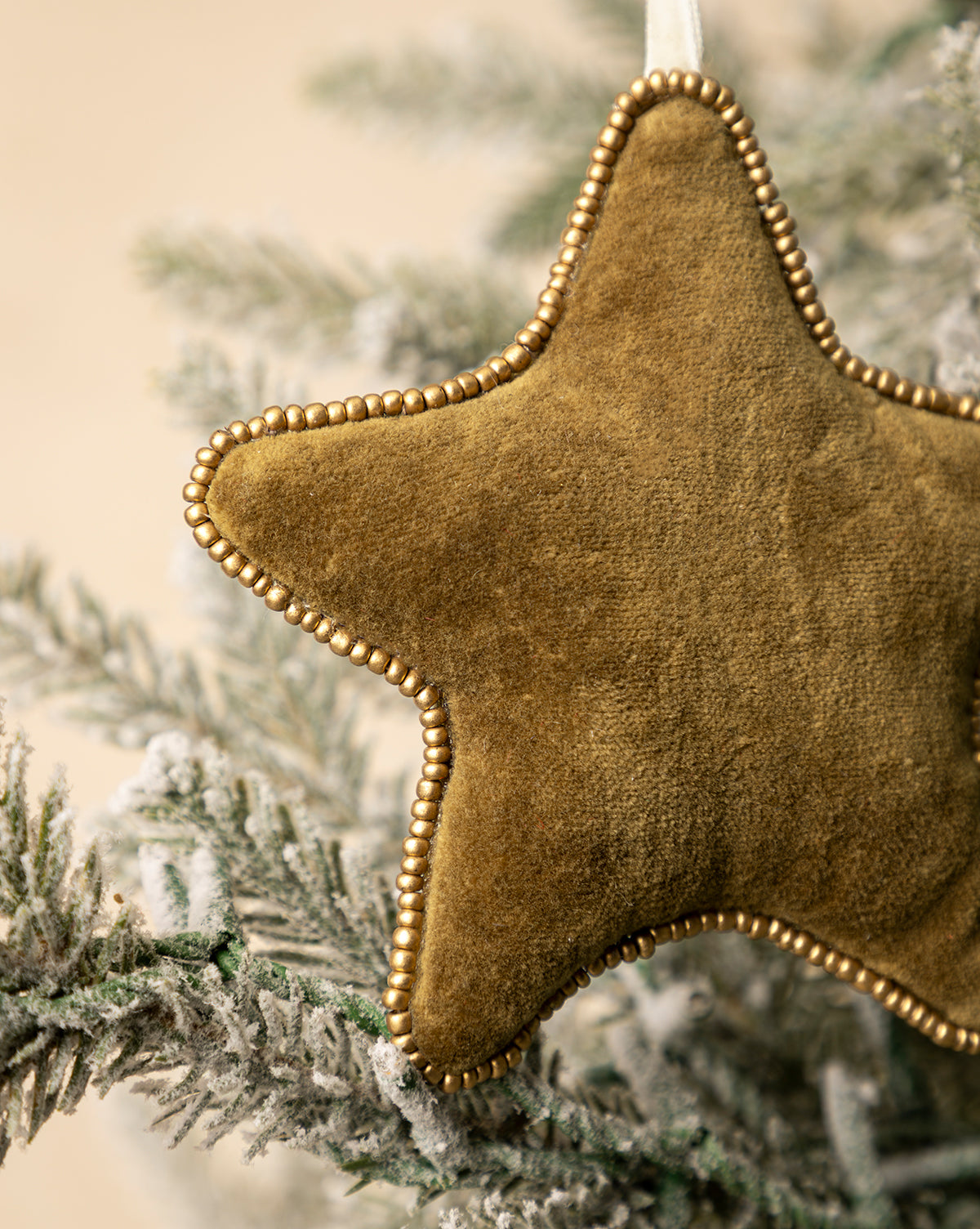 A close-up of the Plush Beaded Star Ornament showcases its beaded edges and festive style as it hangs from a frosted holiday tree branch, by McGee & Co.