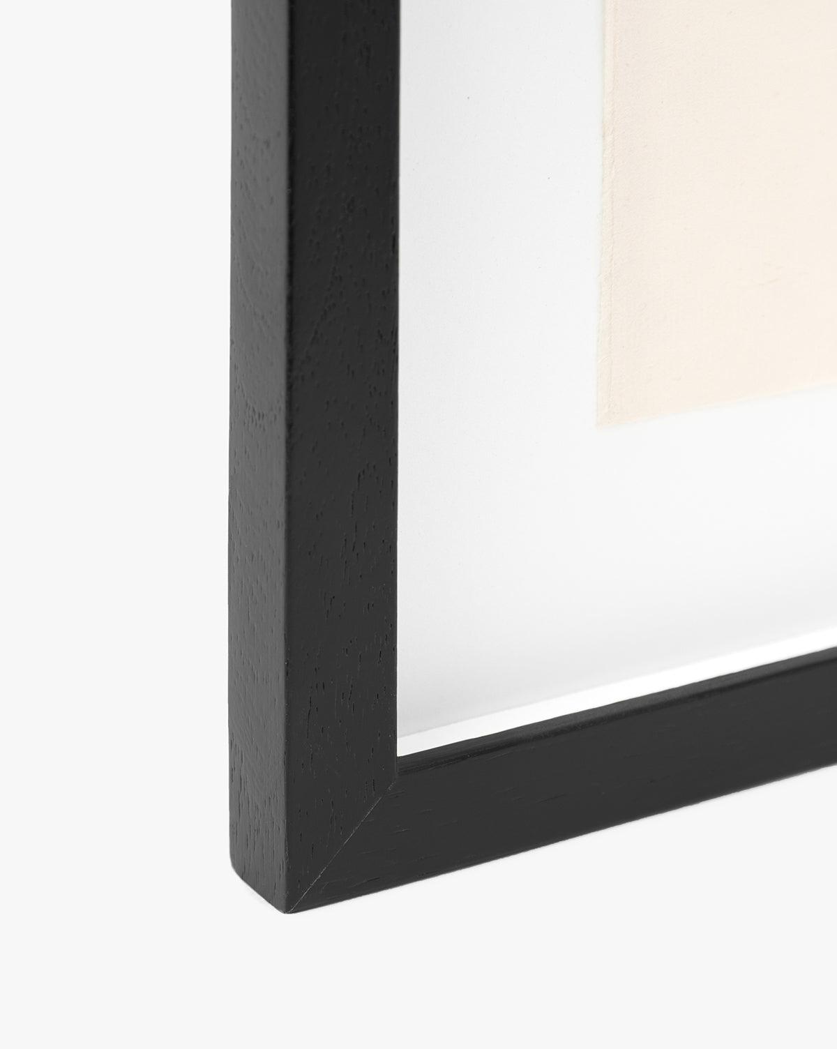 Close-up of the black Point Vicente wooden picture frame corner against a white background, highlighting the edge of the glass and a glimpse of vintage wall art inside.