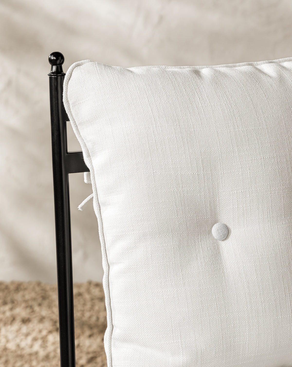 A close-up of a white, tufted cushion with a center button in performance fabric is shown on the Pomeroy Outdoor Dining Chair, set against a softly blurred beige and light brown background by McGee & Co.
