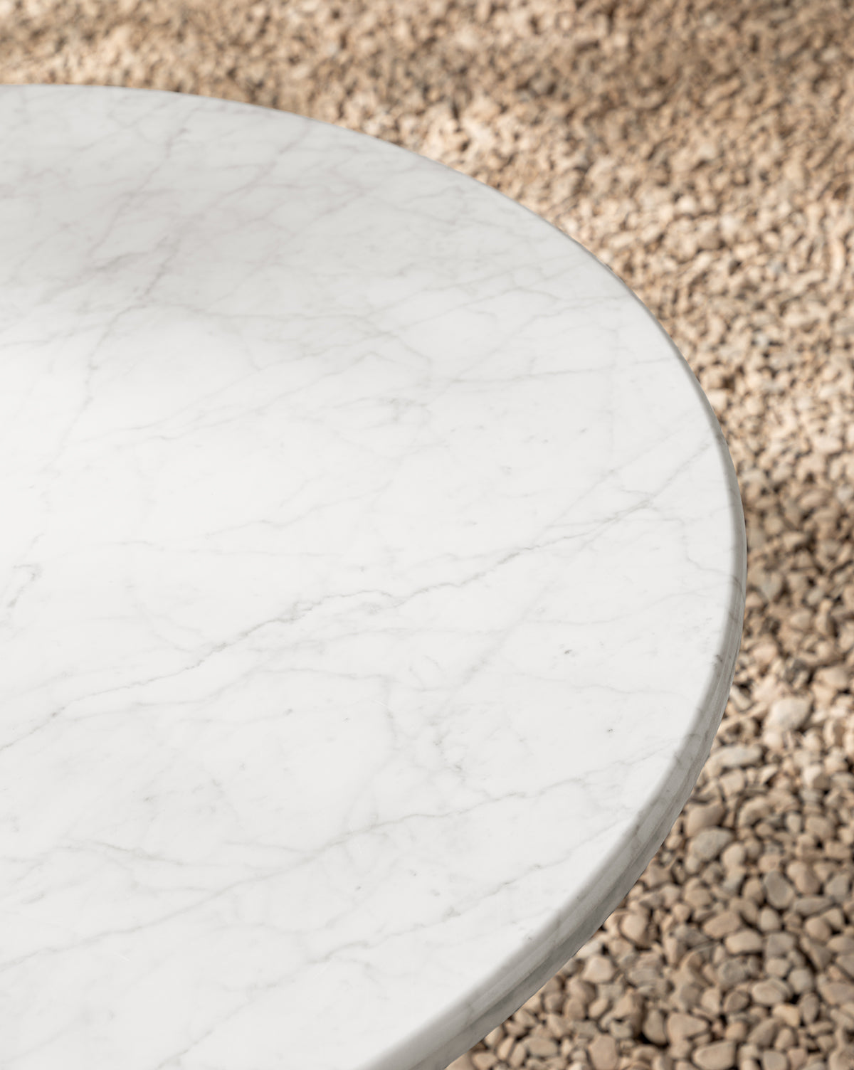 The Pomeroy Outdoor Bistro Table, featuring a round white marble top with subtle grey veining, stands over light-colored pebbles—an ideal choice for adding luxury style to your patio, by McGee & Co.