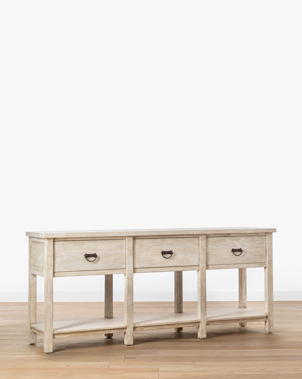 The Martha Sideboard, crafted from reclaimed Douglas Fir, features three drawers with black metal handles and a lower shelf. This rustic light wood sideboard stands on a wooden floor against a plain white background, by McGee & Co.