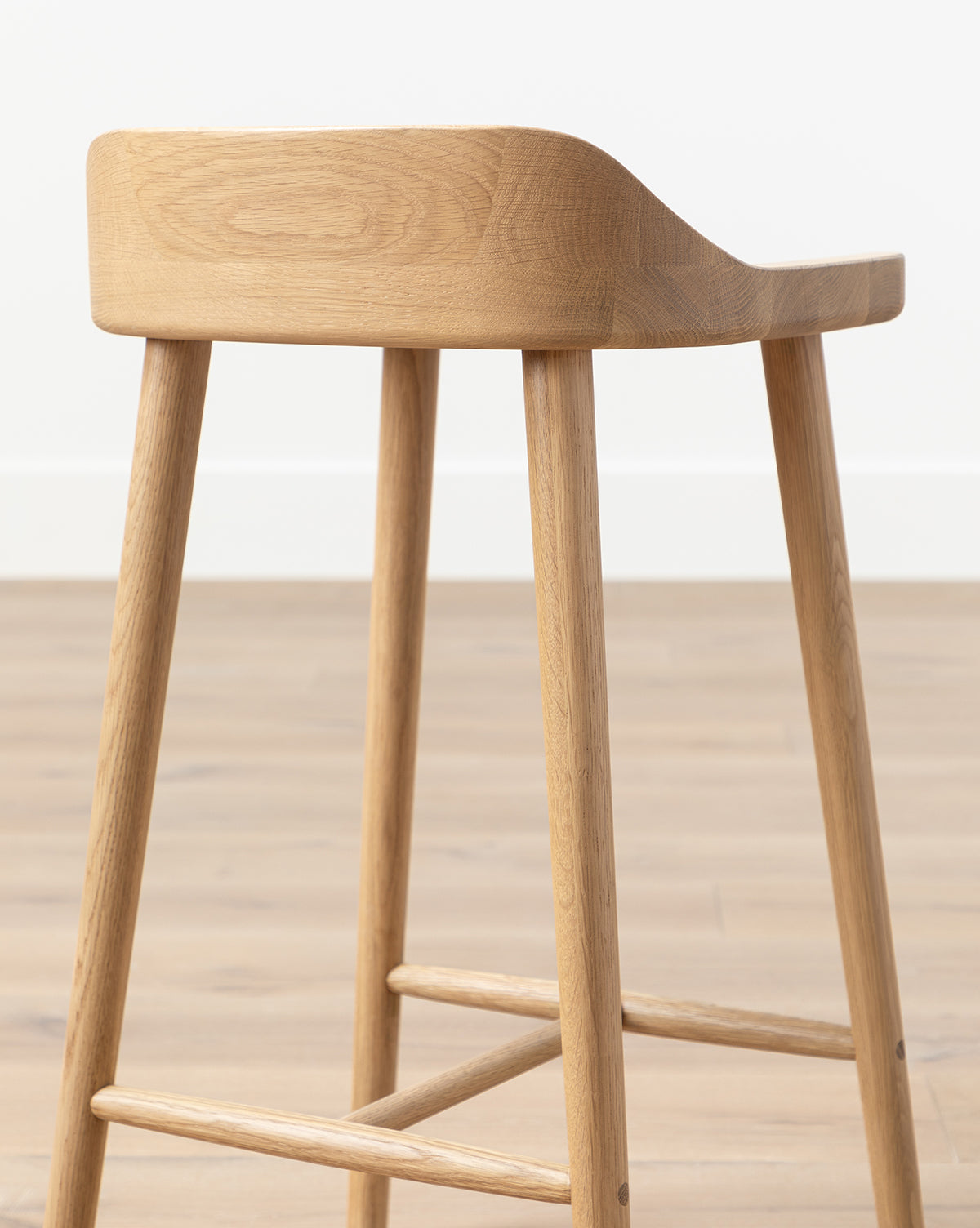 The Makerspalm Portland Counter Stool, featuring four legs and a curved low backrest, sits on a light wood floor against a white wall—perfect for adding style to any kitchen. McGee & Co.