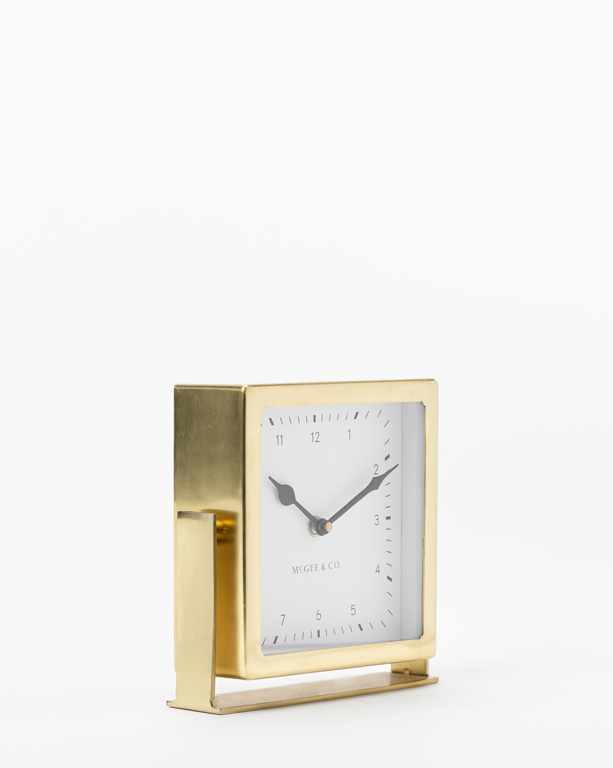The Posey Table Clock is a square gold table clock with black hour and minute hands set at 10:09, a white face with minimal black markings, and stands on a flat base against a plain white background.