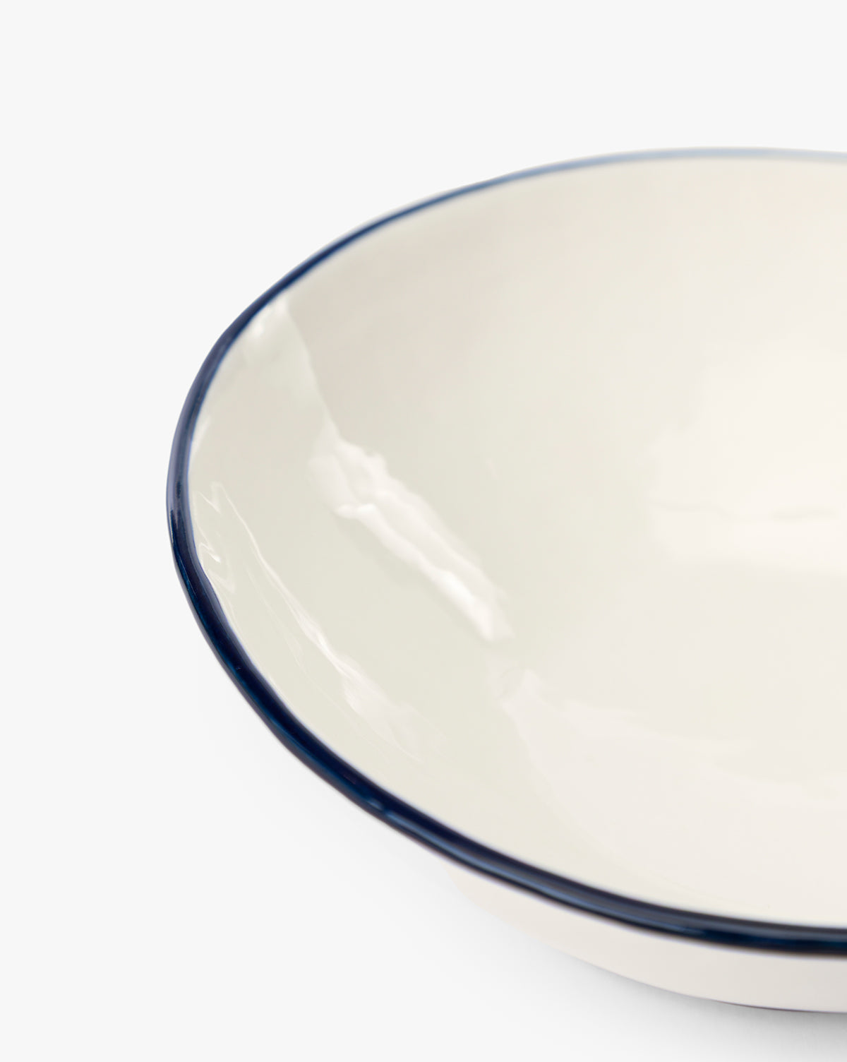 Close-up of a white enamel Pritchard Bowls (Set of 4) with a navy rim and creamy glaze, shown against a plain white background. Only part of the bowl’s edge is visible, by McGee & Co.