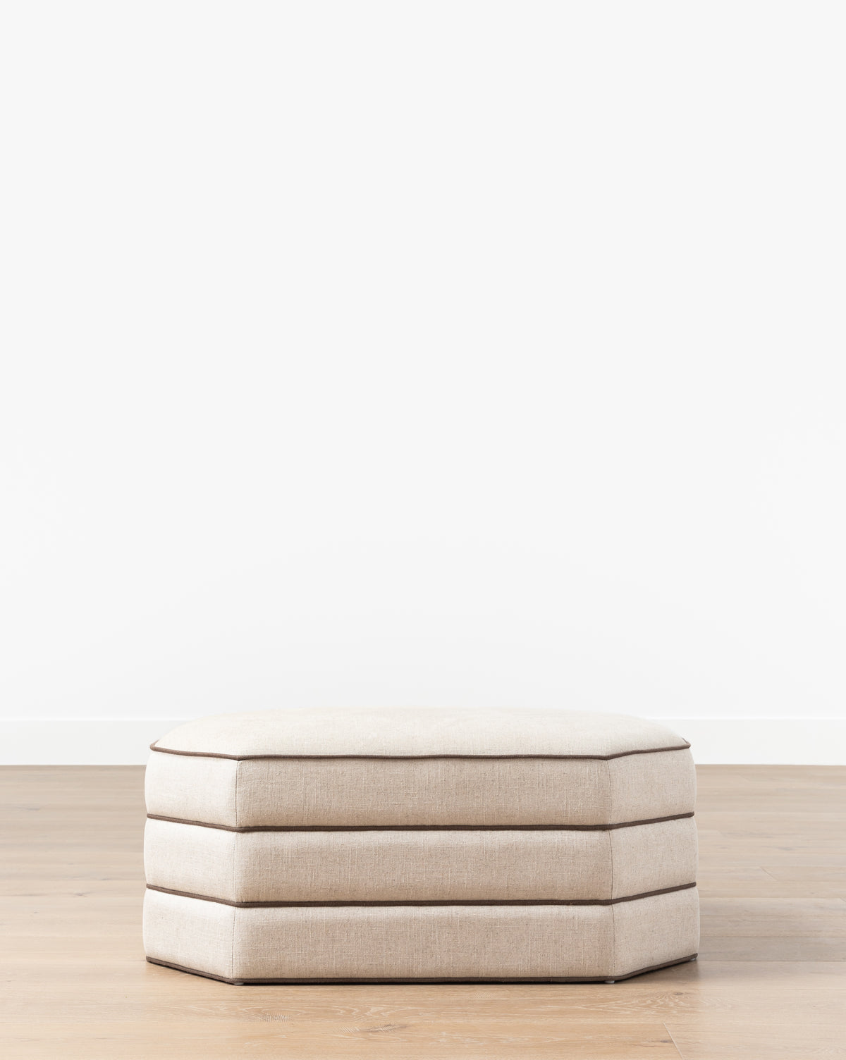The Makerspalm Rafferty Ottoman, a beige rectangular piece with layered performance linen cushions, is set on a light wood floor against a plain white wall. McGee & Co.