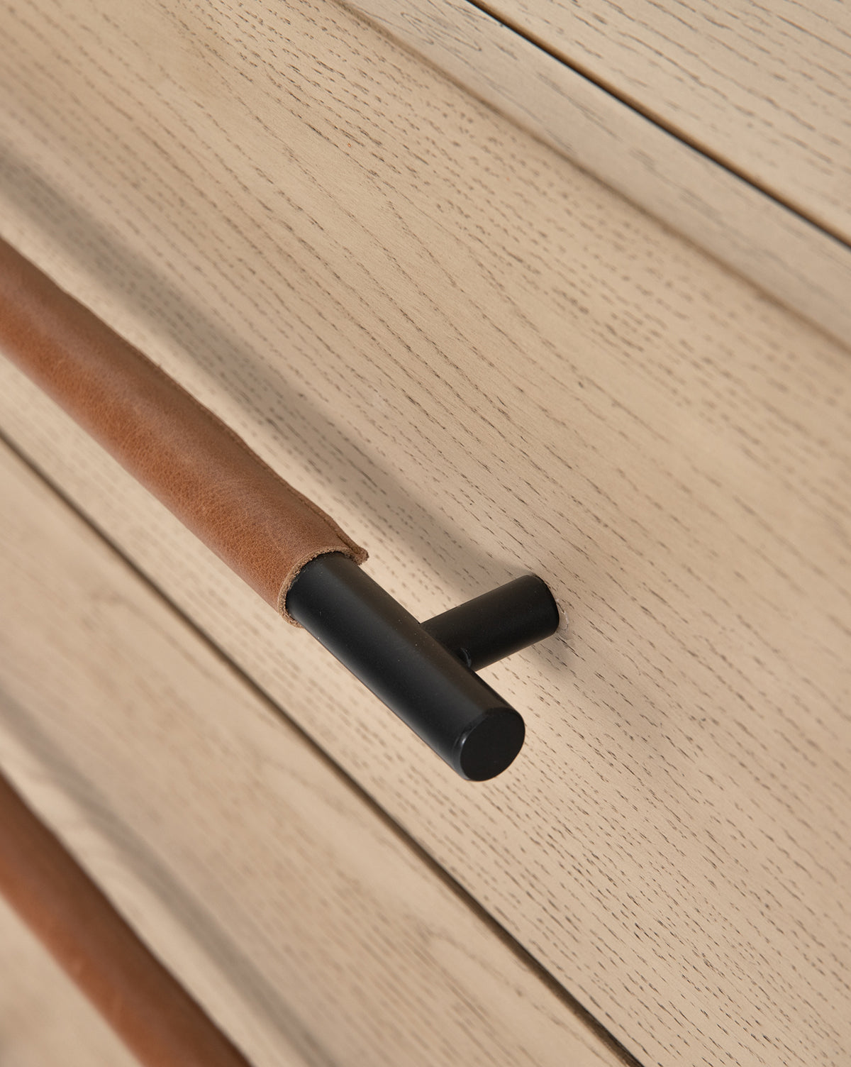 Close-up of a Ralston 6-Drawer Dressers light oak drawer, showing visible wood grain and a black metal handle wrapped in brown leather, mounted horizontally.