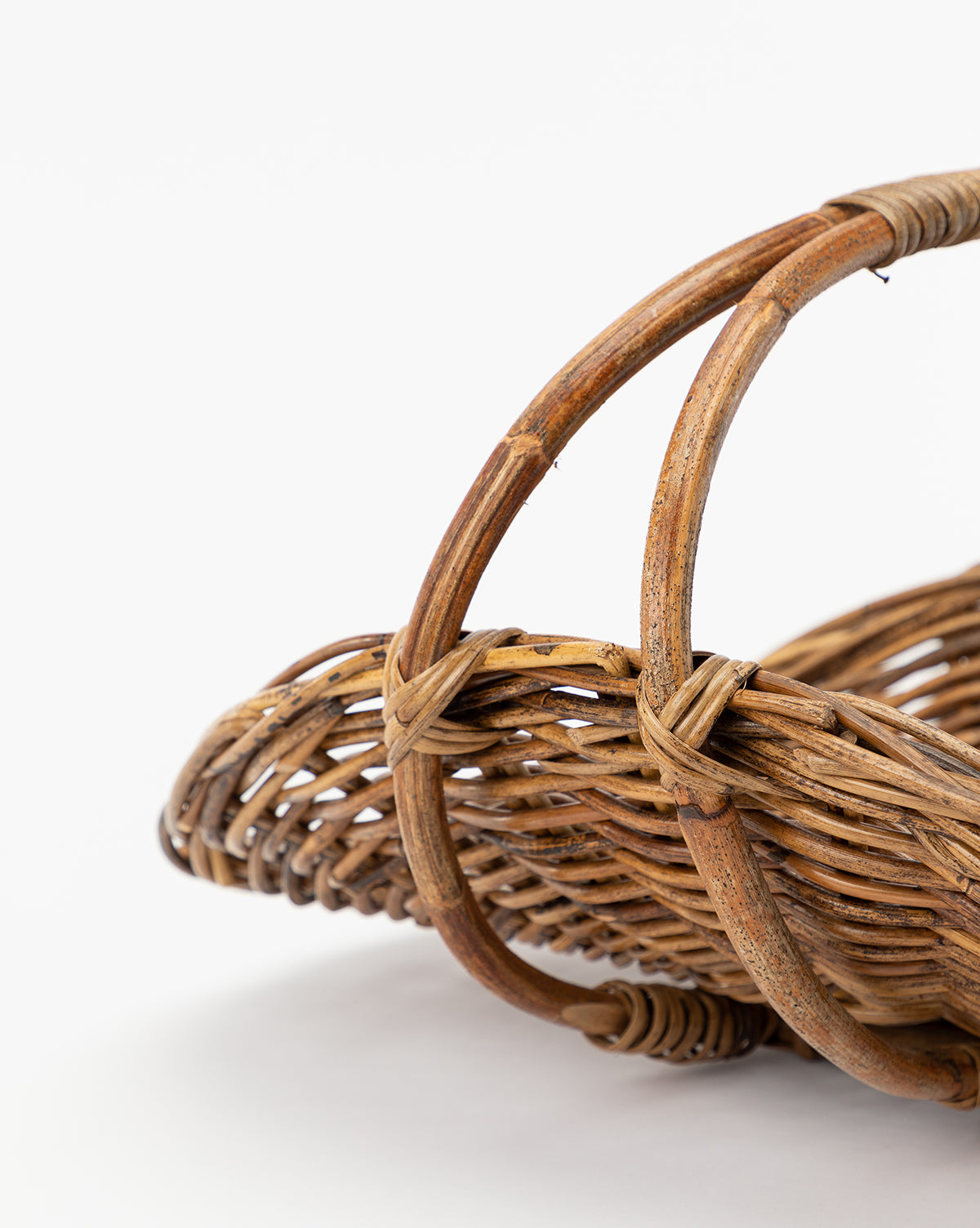 Close-up of the Rattan Gardening Tray, featuring its woven wicker texture and curved handle. The natural, organic look is highlighted against a plain white background with only part of the tray visible.
