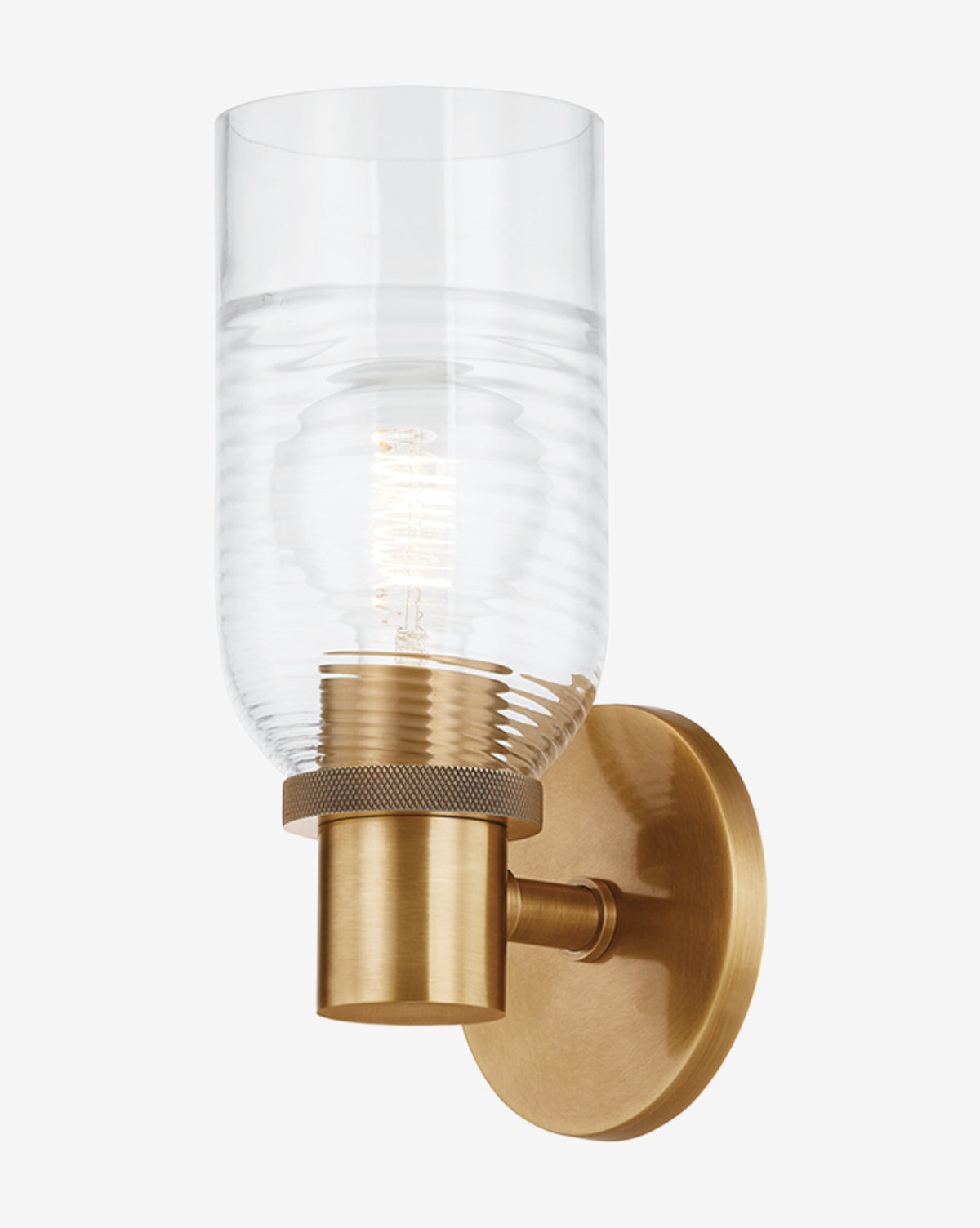 The Redding Sconce by Troy Lighting features a cylindrical ribbed glass shade, patina brass base, and exposed bulb, all mounted on a round brass wall plate set against a white background. McGee & Co.