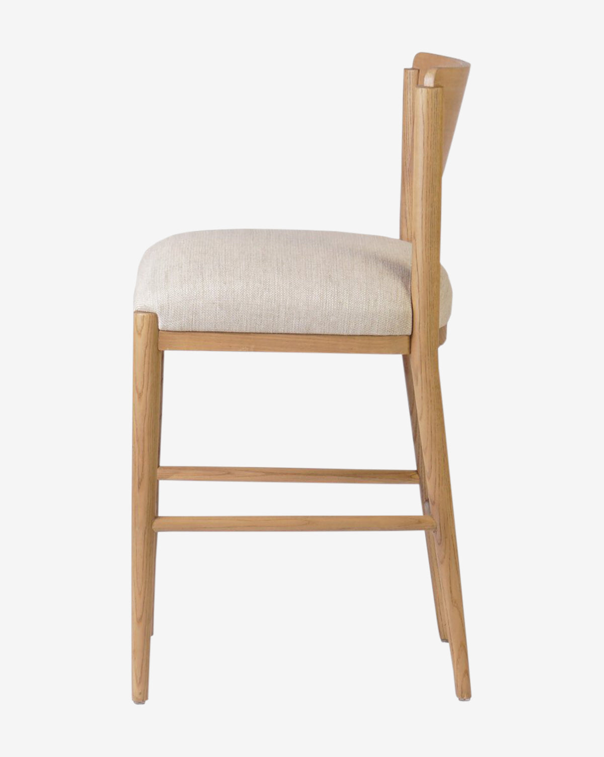Side view of the Reverie Stool by Four Hands, a modern wooden chair for kitchens featuring a light beige cushioned seat, angled backrest, clean lines, and a natural wood finish. McGee & Co.