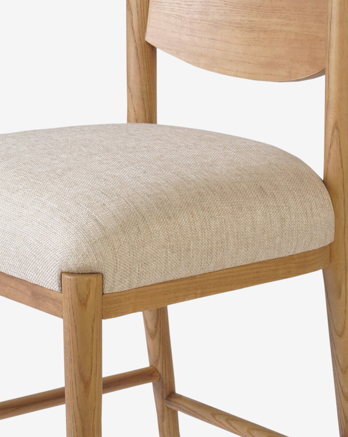 Close-up of the Four Hands Reverie Stool, showcasing its natural wood frame, light beige upholstered seat, and curved backrest—an ideal modern kitchen accent—set against a plain white background. McGee & Co.