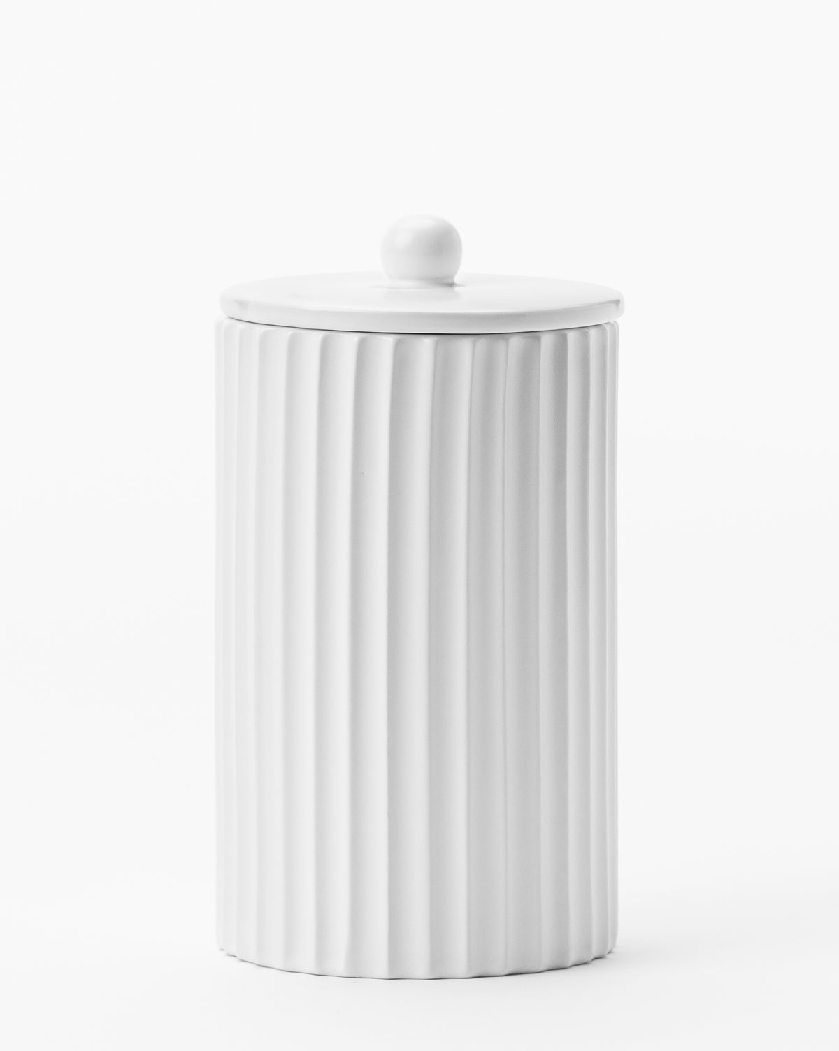 The Fluted Lidded Bathroom Canister is a tall, white ceramic jar with vertical ridges and a round-handled lid, designed as a stylish bathroom accessory and shown here against a plain white background.