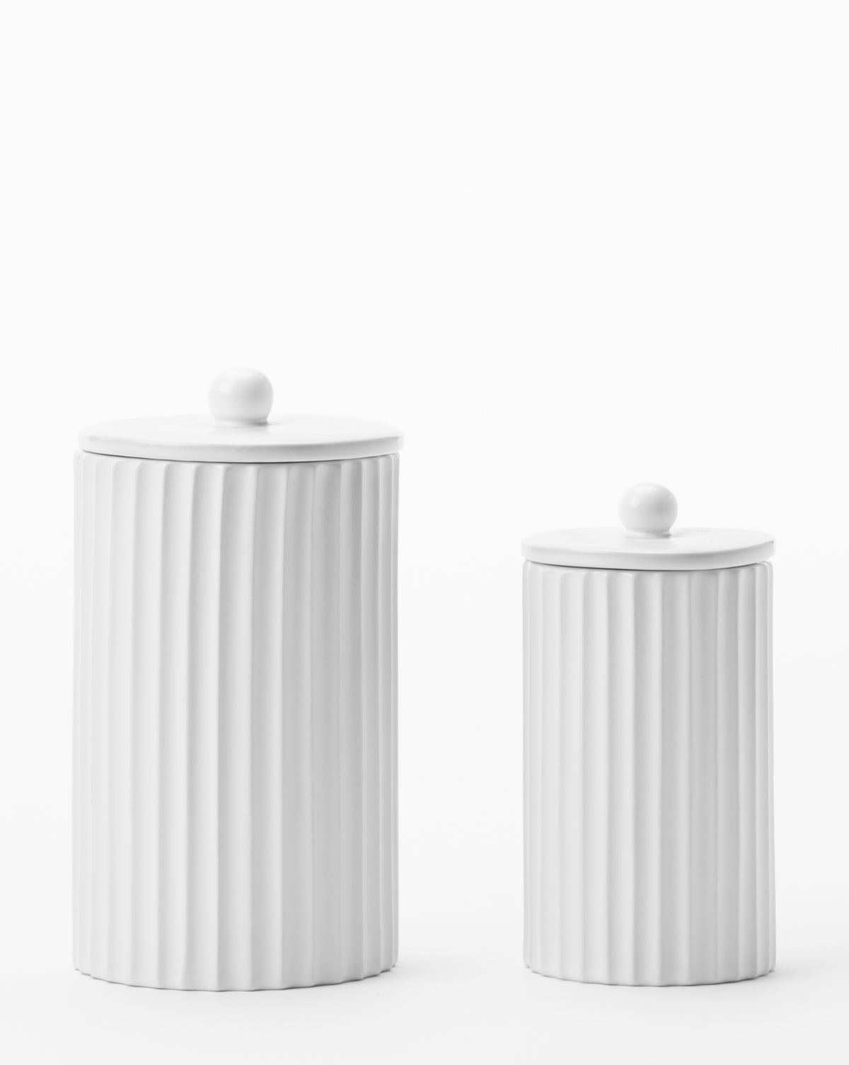 The Fluted Lidded Bathroom Canister set features two white ceramic canisters—one tall, one short—with vertical ribbed patterns and round knobs, adding elegance to any bathroom décor.