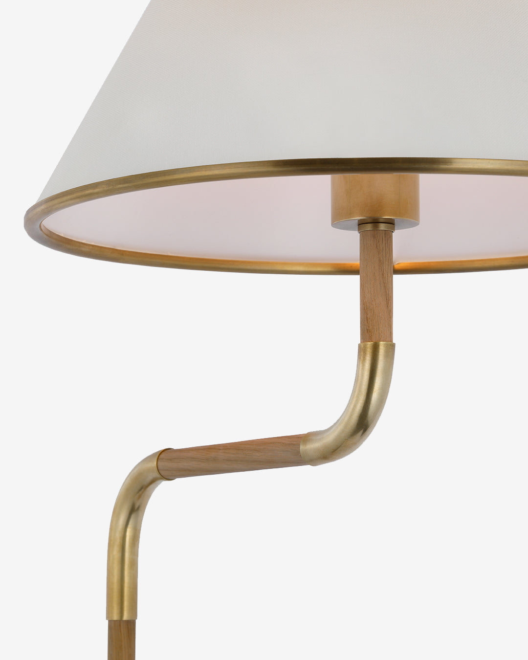 A close-up of the Rigby Medium Bridge Arm Floor Lamp, showcasing its white linen shade with a brass rim and a curved wood and brass stem, set against a plain white background, by McGee & Co.