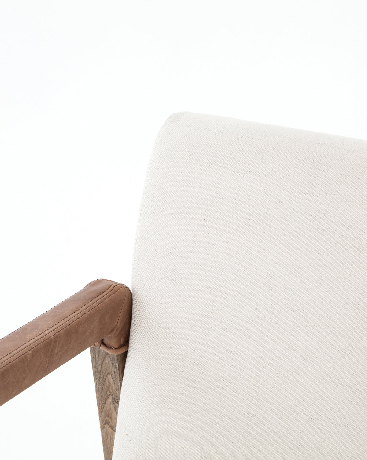 A close-up of the Robby Dining Armchair’s backrest and armrest, showcasing light beige linen blend upholstery with a wooden armrest partially wrapped in tan leather against a plain white background, by McGee & Co.
