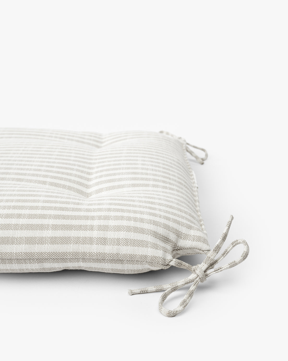 A close-up of the Credence Romany Dining Chair Cushion, featuring light gray and white stripes with two fabric ties, perfect for oak dining chairs, set against a plain white background. McGee & Co.