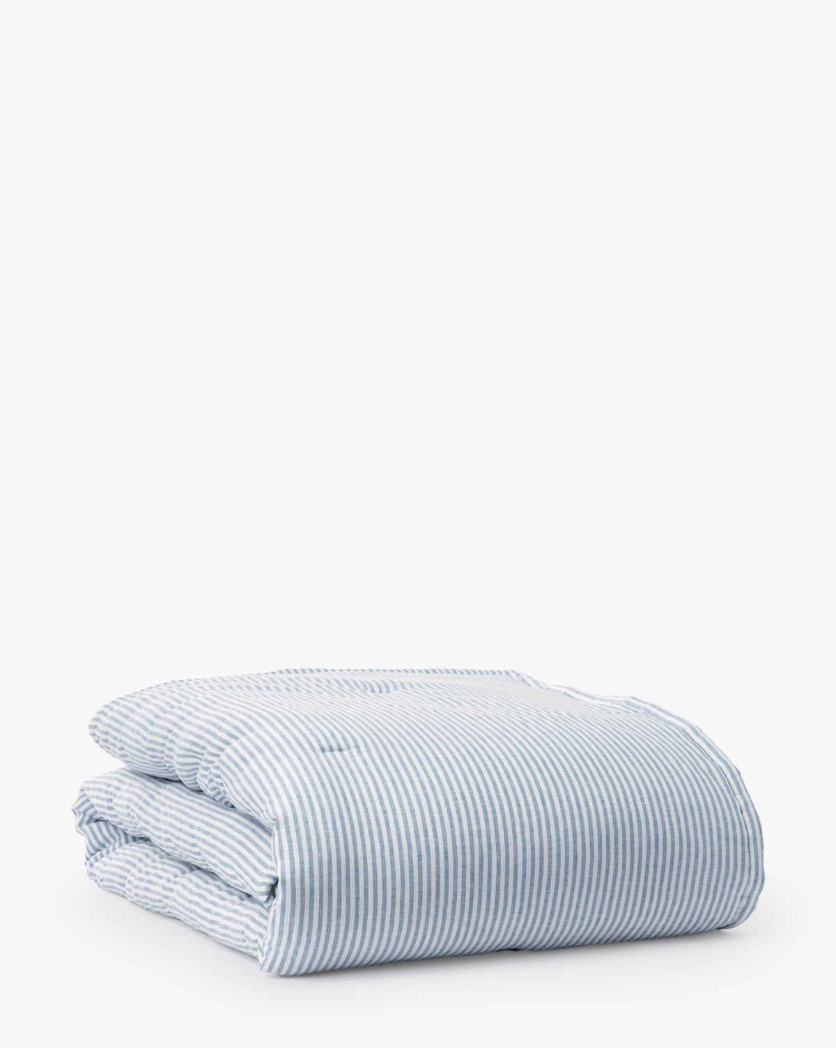 The Rosemary Quilt, featuring blue and white stripes, is neatly folded on a white background to highlight its stylish linen and cotton blend bedding.